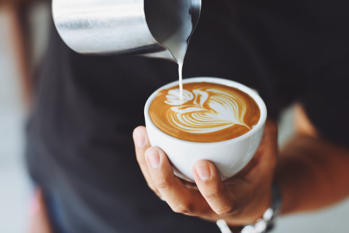 Someone pours a latte into a cup with latte art.